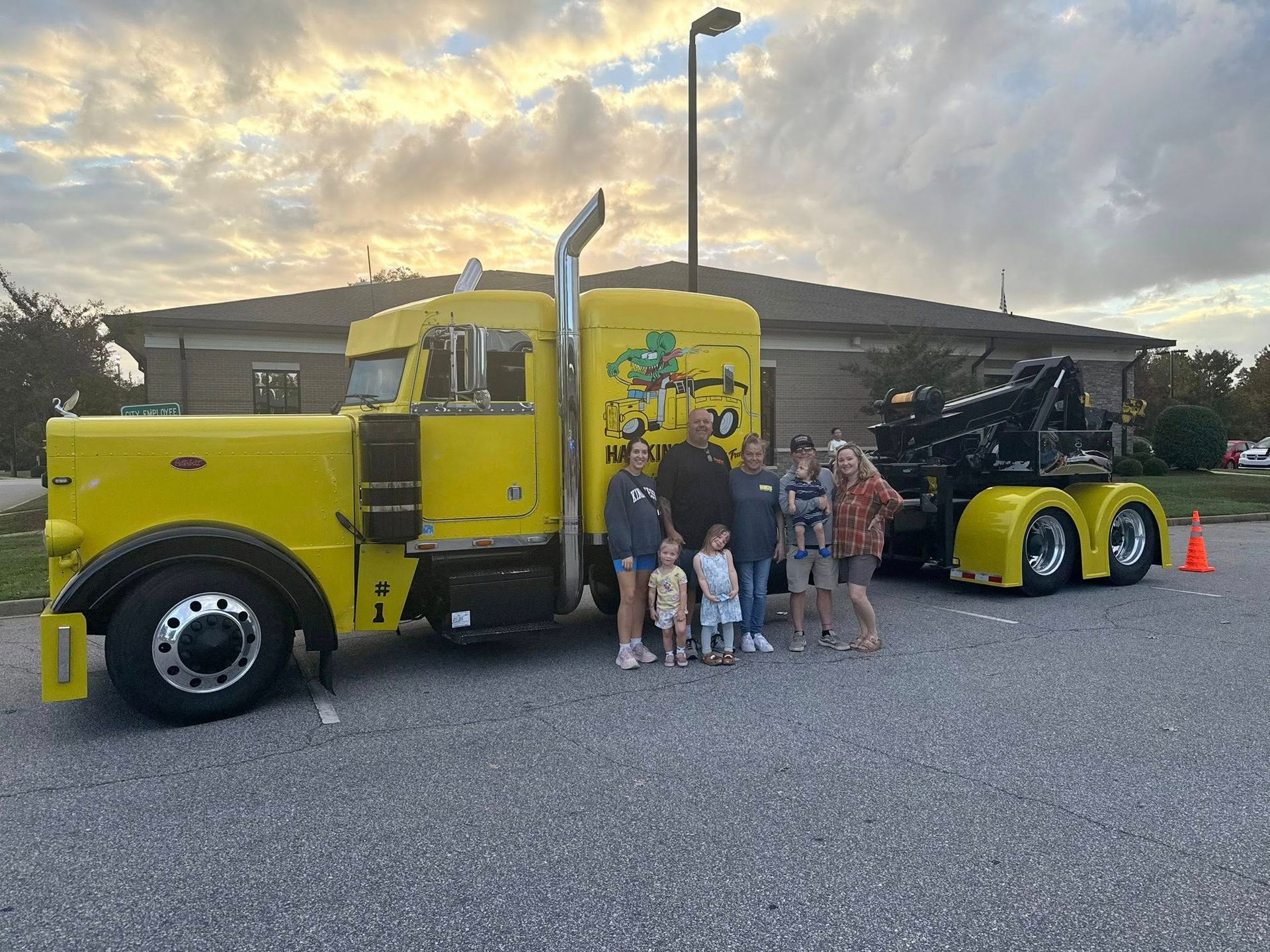Yellow truck with people posing beside it at dusk in a parking lot