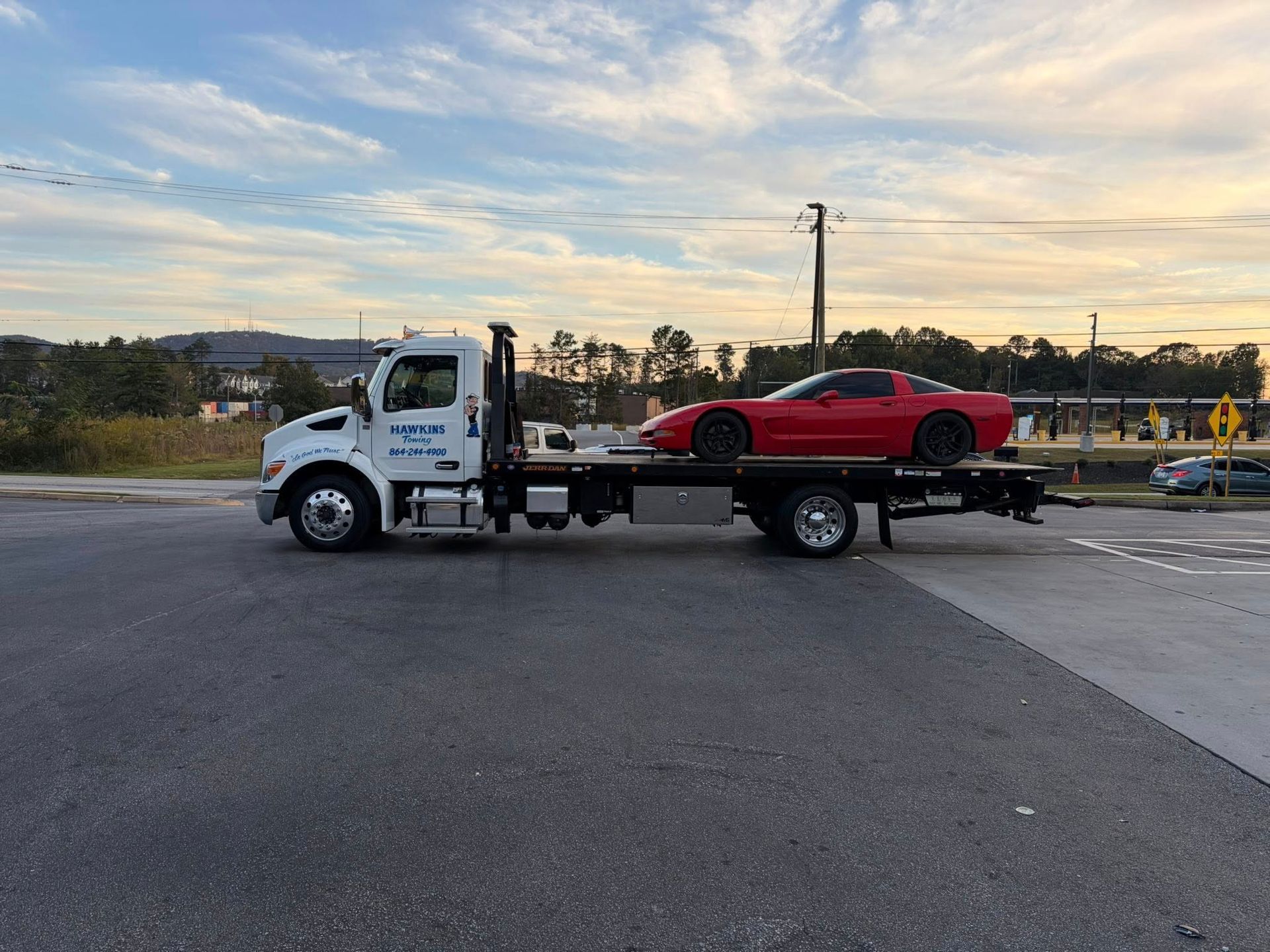 Tow truck hauling a red sports car on a flatbed at dusk on a roadside