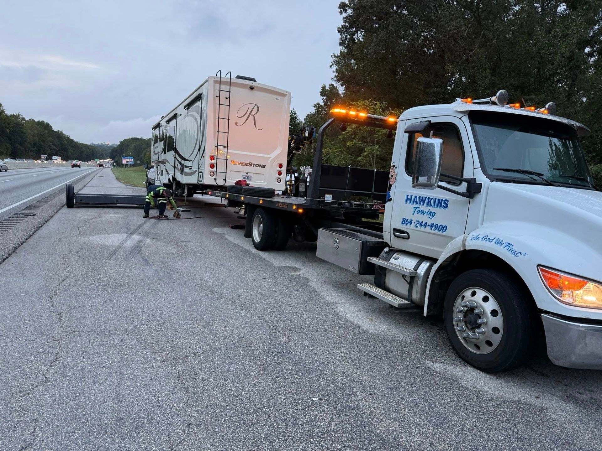 Tow truck towing a damaged box truck on a highway shoulder at dawn