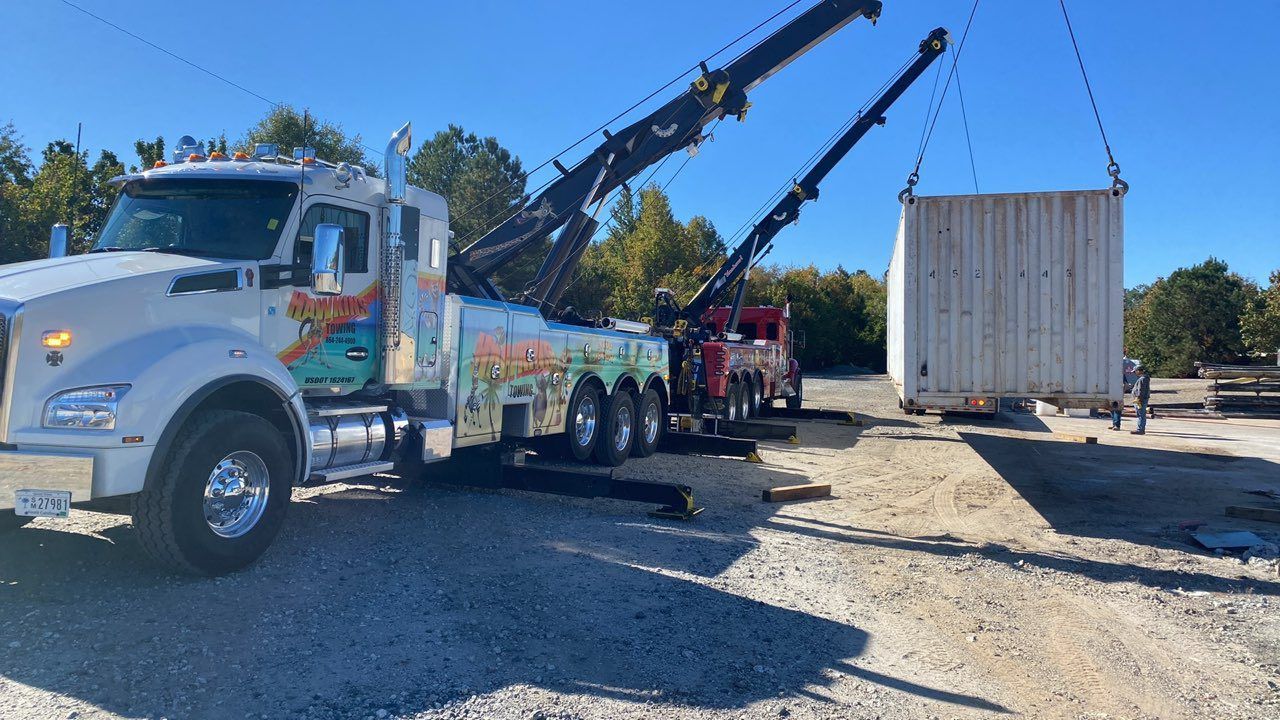 Tow truck lifting a white shipping container beside a gravel lot under a clear sky