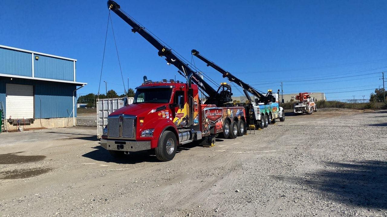 Red tow truck carrying a row of damaged vehicles on a gravel lot under a clear blue sky