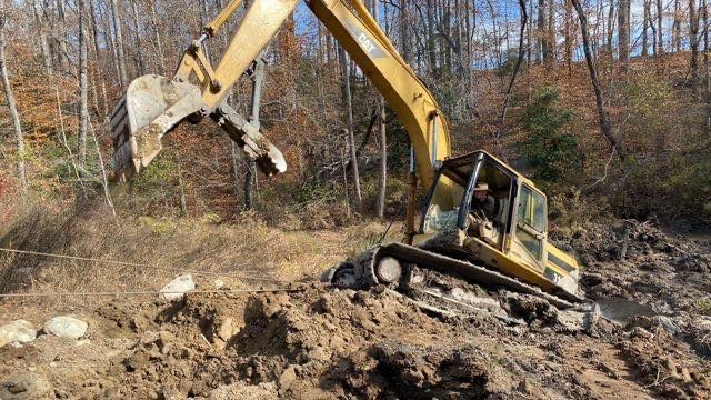 Yellow excavator on muddy hillside lifting debris in a wooded area