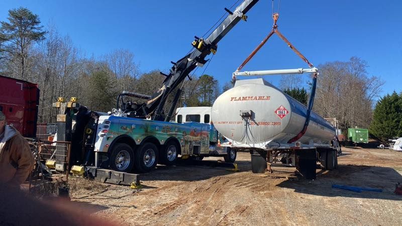 Crane lifting a white cylindrical tank onto a trailer in a muddy outdoor worksite