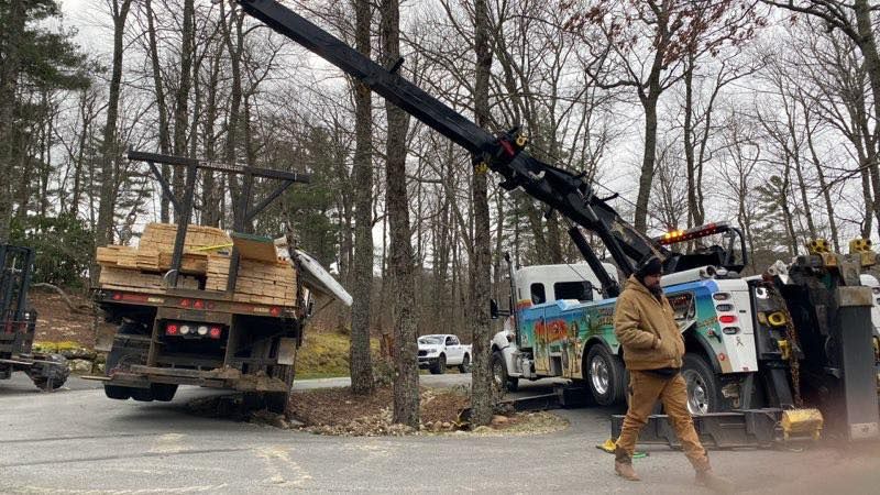 Utility crew using a crane to lift a truck load of wooden beams on a roadside in a wooded area