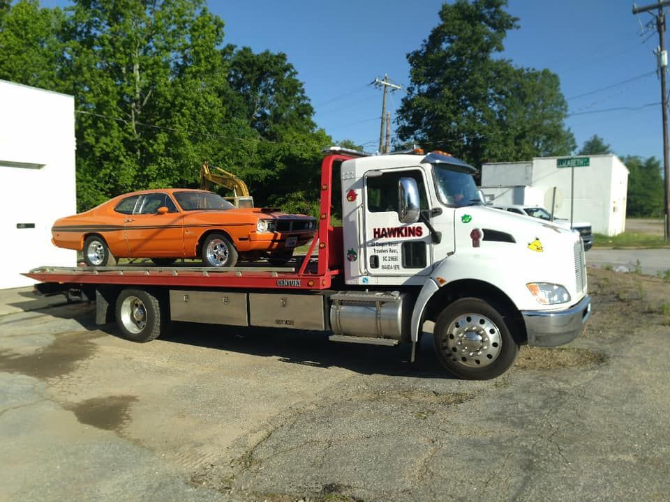 Tow truck hauling an orange car on a flatbed in a sunny parking lot