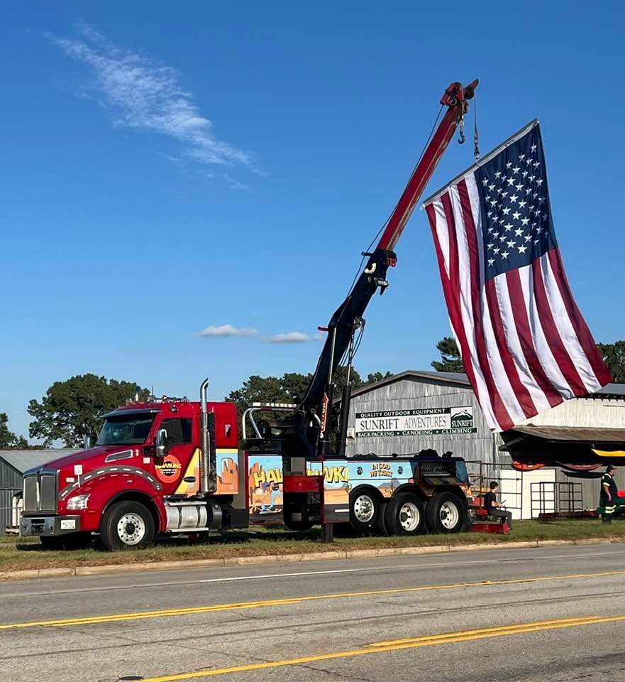 Red fire truck with extended crane beside a large American flag under a blue sky.