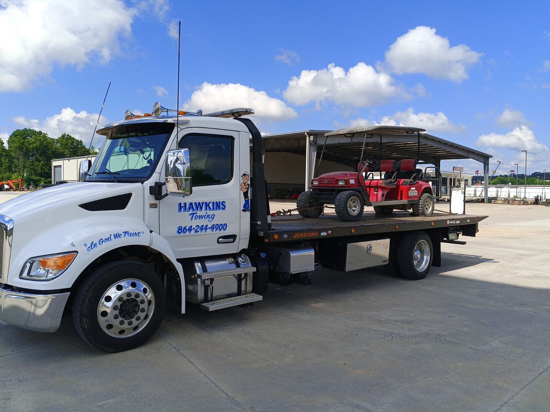 White flatbed tow truck carrying a red ATV on a sunny lot under blue sky