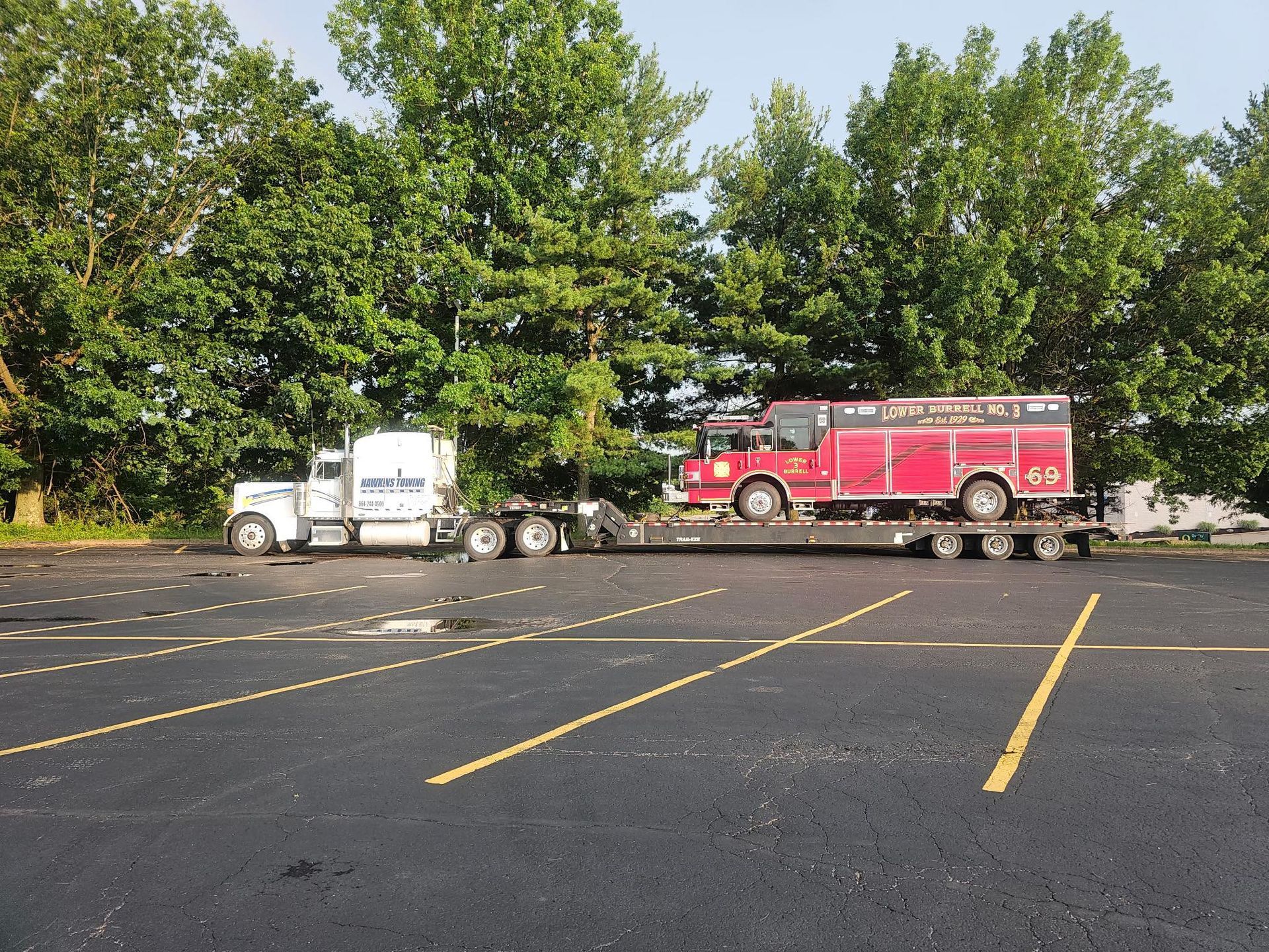 White semi truck with red trailer parked in a nearly empty lot by trees