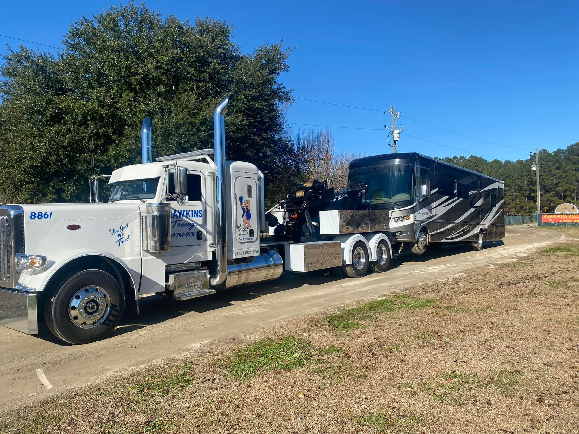 White semi truck hauling a black trailer parked on a grassy roadside under a clear blue sky