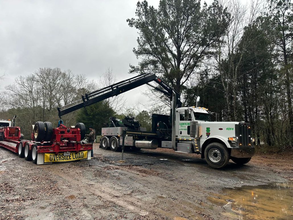 Tow truck lifting a white semi-truck cab in a muddy lot under overcast skies