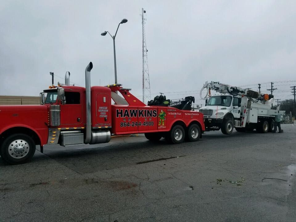 Red tow truck hauling a white utility truck on a wet road under a gray sky