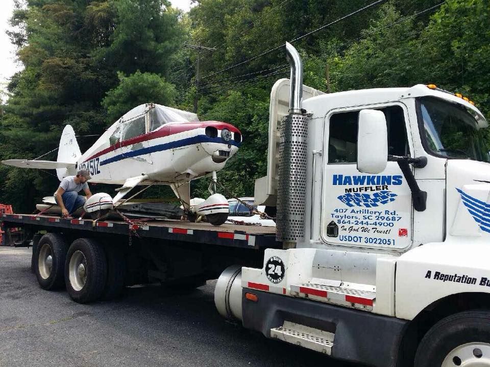 Small plane on a flatbed truck with a driver’s cab, parked outdoors under cloudy skies