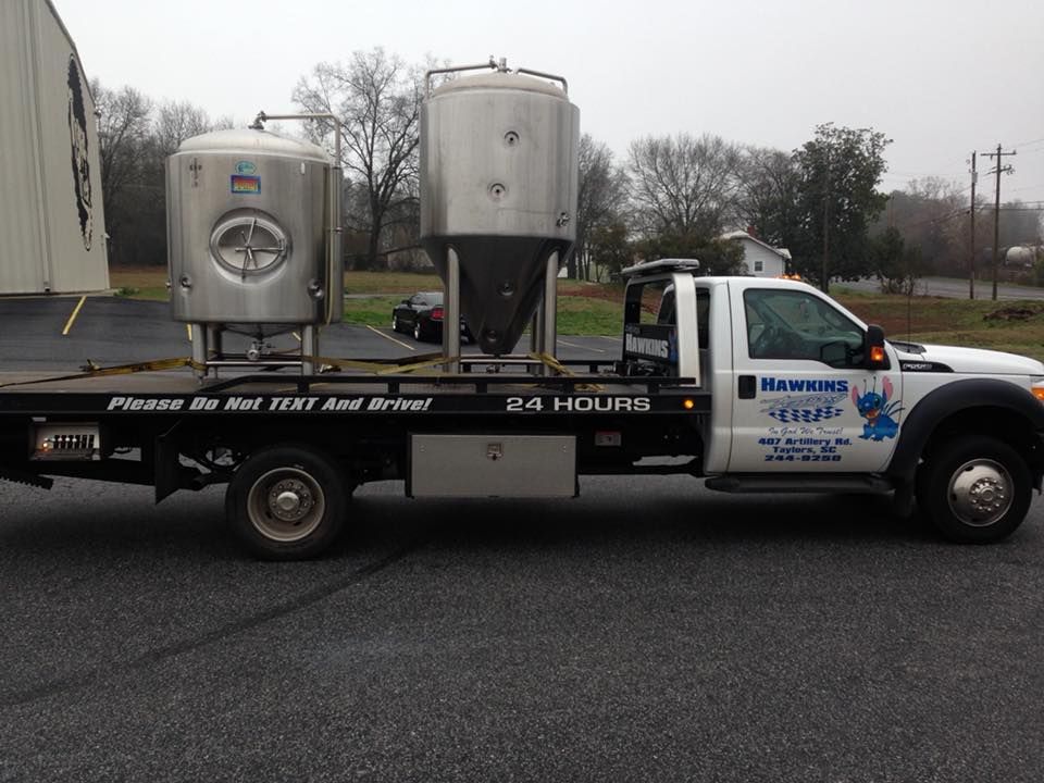 Silver beverage truck with large metal tanks parked on a road overcast day