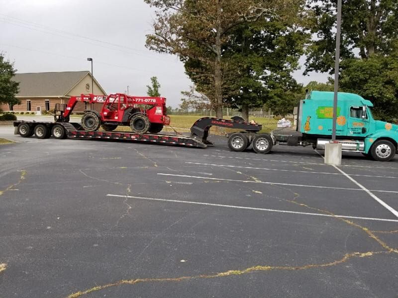 Teal semi truck towing a flatbed trailer with a red tractor in a parking lot