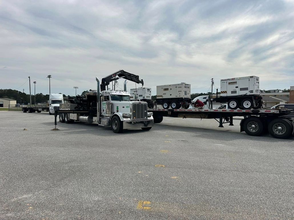 Tow truck hauling a flatbed trailer in a gravel lot under a cloudy sky