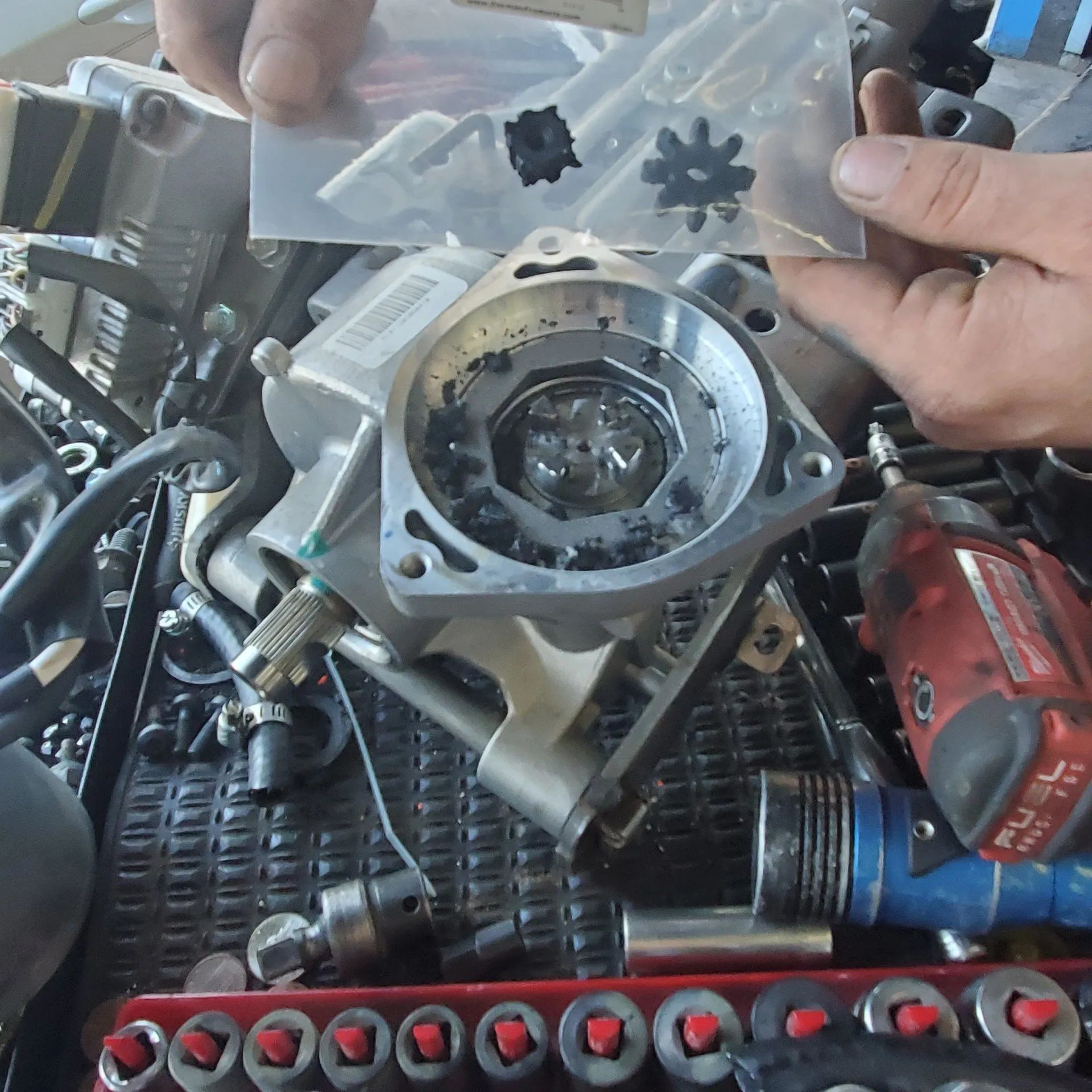 Hands holding small black parts over a metal engine component and tools on a workbench