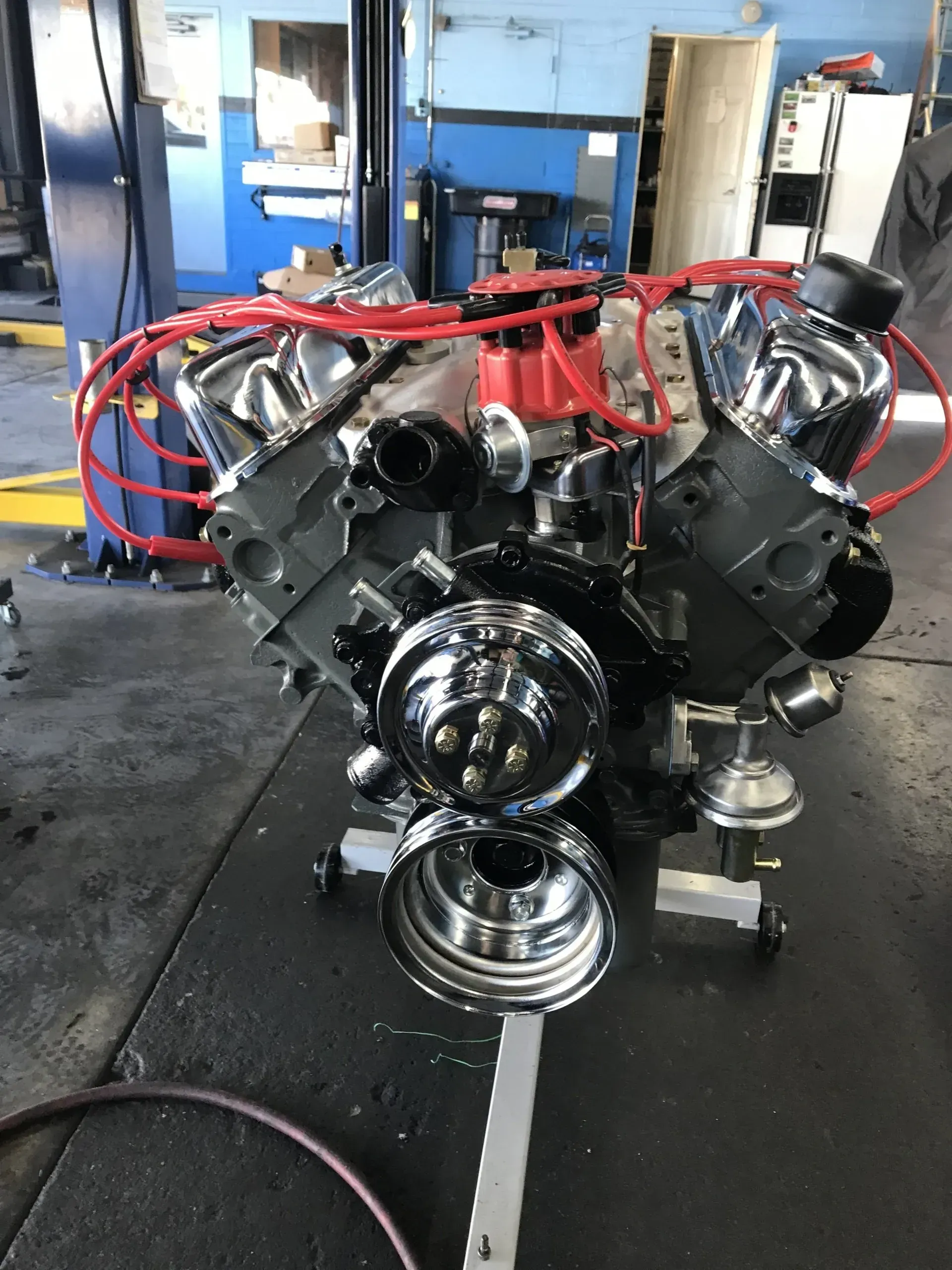 Large black engine block on a workshop floor with red hoses and blue equipment in the background