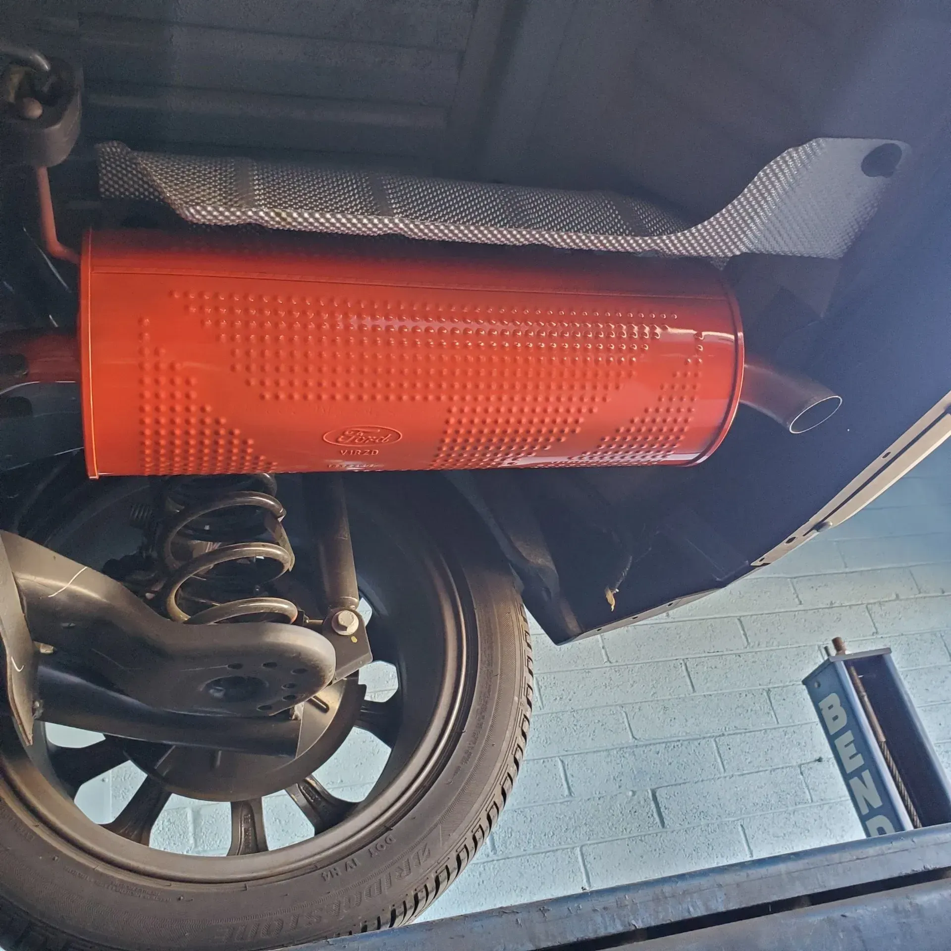 Orange exhaust muffler beneath a car near the rear wheel, seen from underneath.