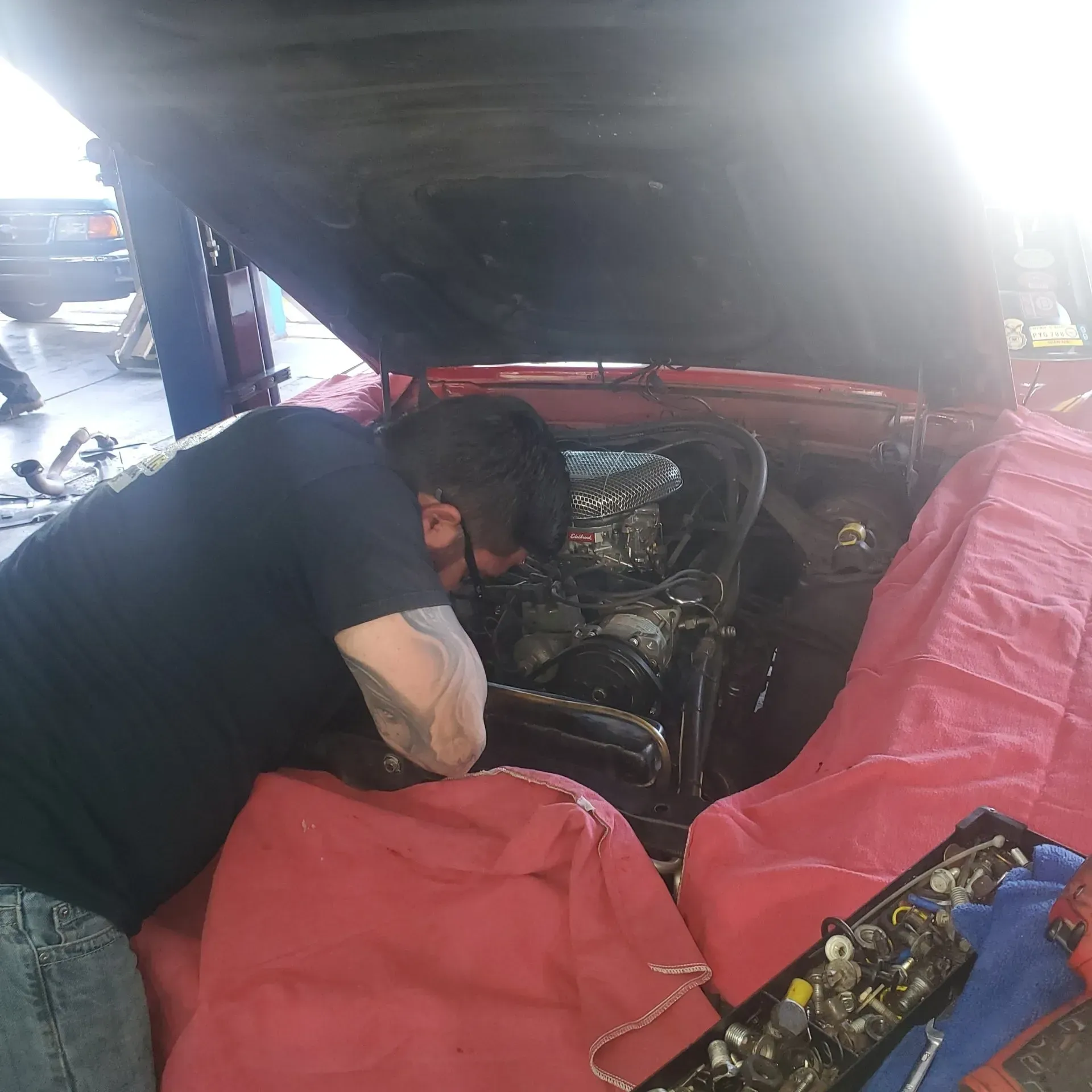 Mechanic working under a red car hood in a garage, inspecting the engine.