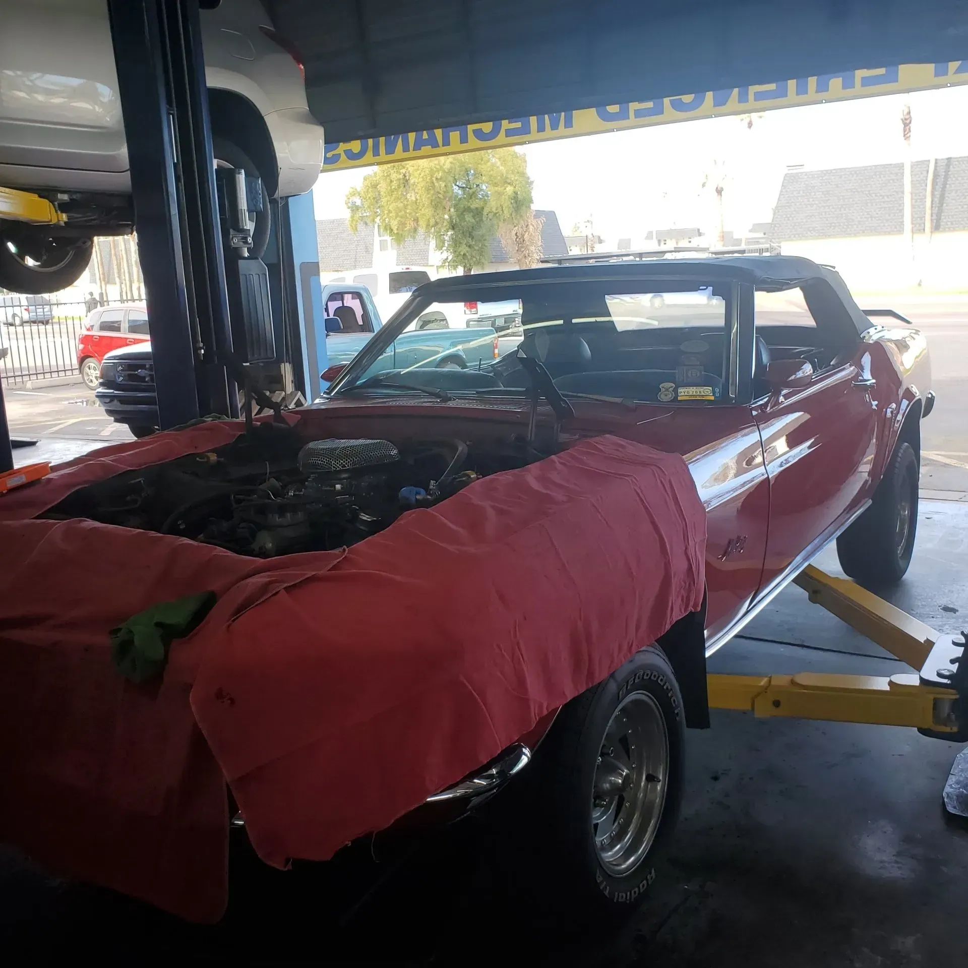 Red convertible in auto shop, hood covered with a red blanket, on a car lift.