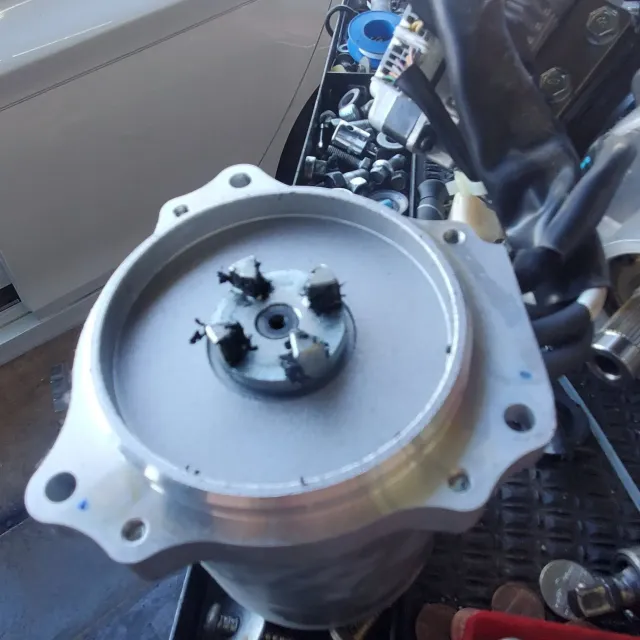 Close-up of a silver metal engine part with bolts and a black central shaft on a vehicle floor