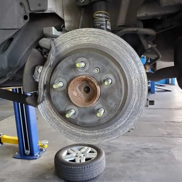Car wheel removed on a lift, with brake rotor visible and a tire lying on the garage floor.