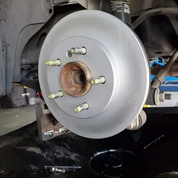 Car wheel brake rotor and hub assembly with lug studs, viewed in a garage during repair