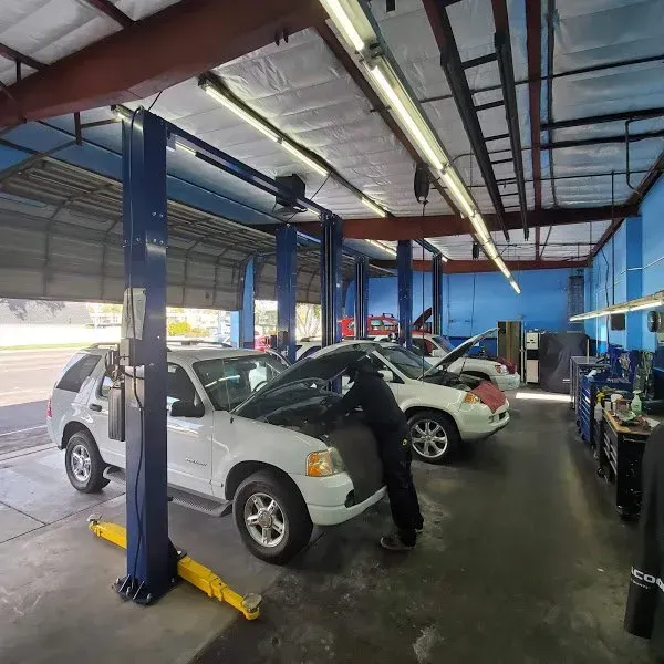 Auto repair shop with cars on lifts and a mechanic working under a white SUV