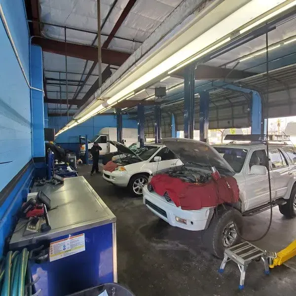 Auto repair shop with several cars, including one with its hood open, under bright blue beams