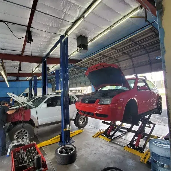 Auto repair shop with two cars on lifts, one red hood open and one white car, plus tools nearby