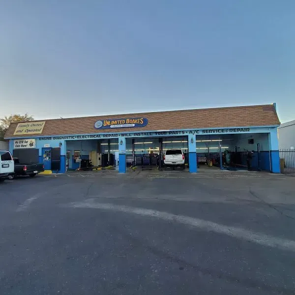 Strip mall storefronts with blue pillars and parked cars under a clear sky