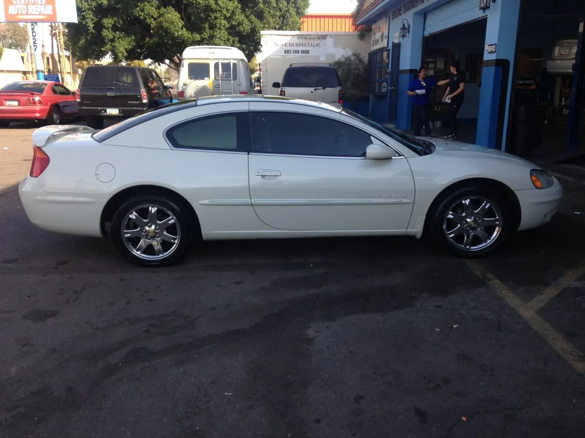 White two-door coupe parked outside a shop garage