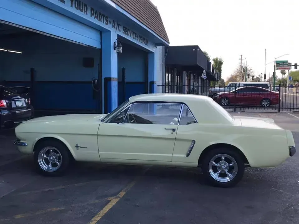 Light yellow classic Ford Mustang parked outside a blue auto shop