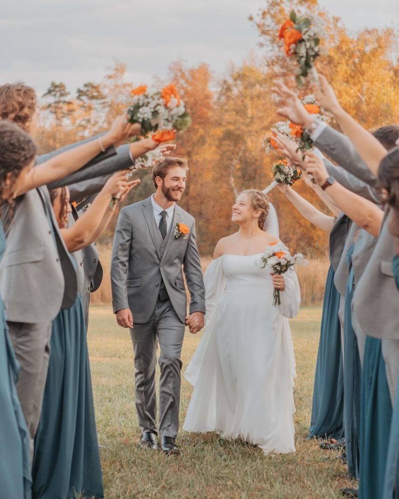 Wedding couple walking through flower confetti tunnel outdoors