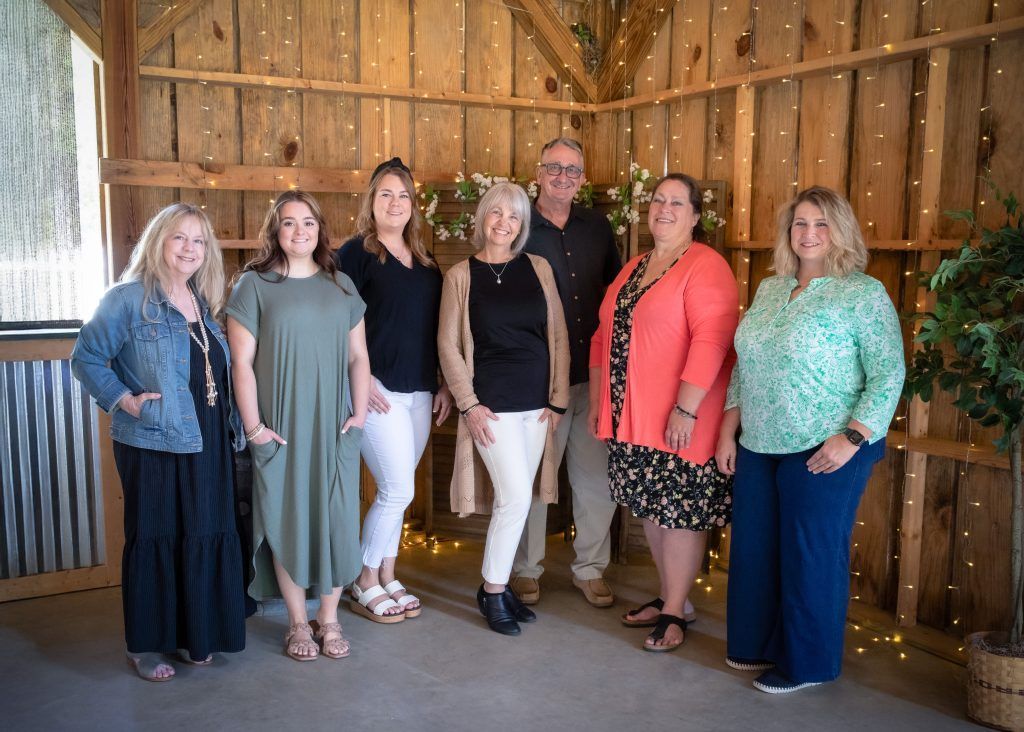 Six people posing indoors against a rustic wooden barn wall, smiling at the camera.