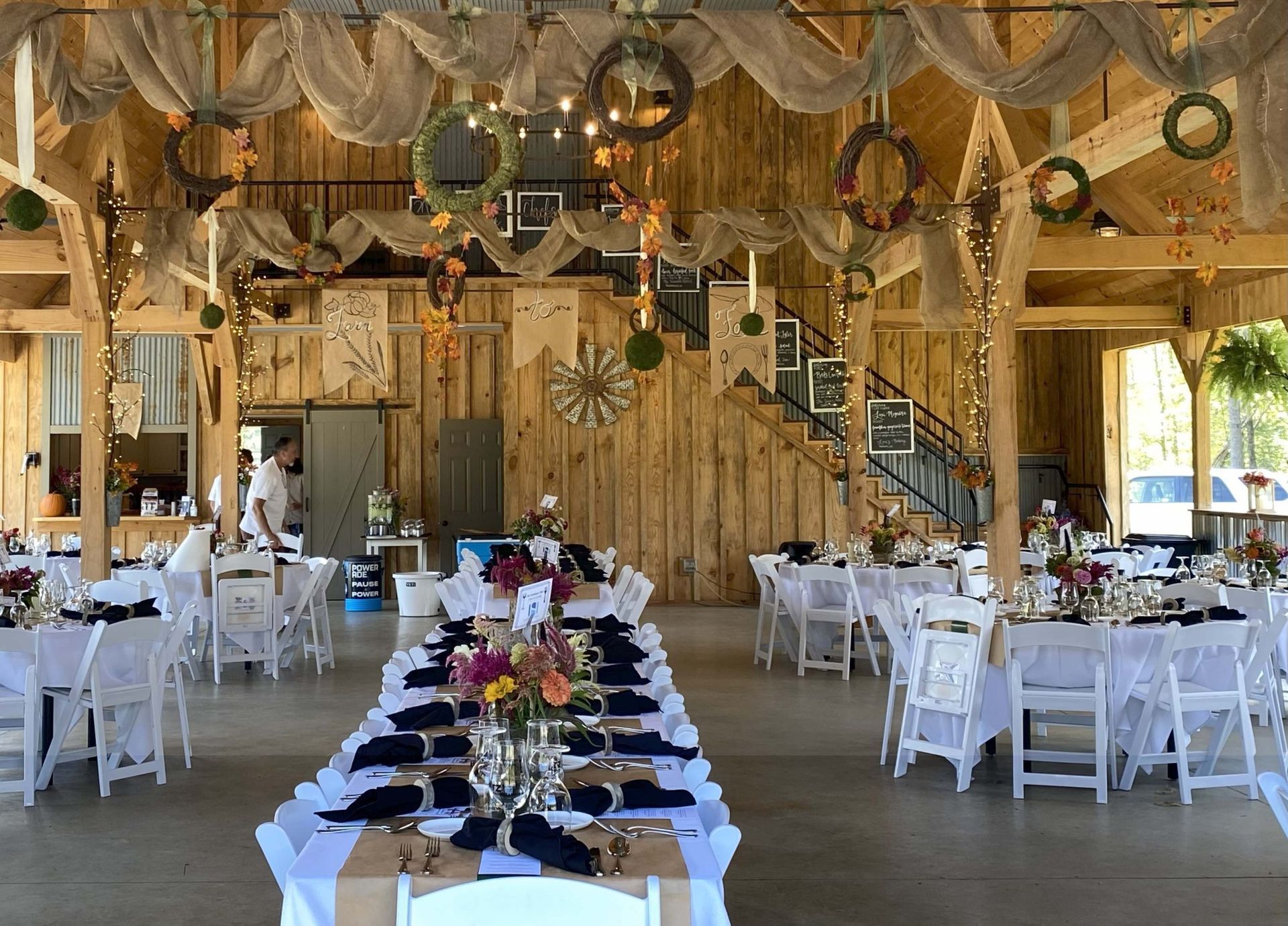 Rustic barn wedding reception setup with white tables, black chairs, and floral centerpieces