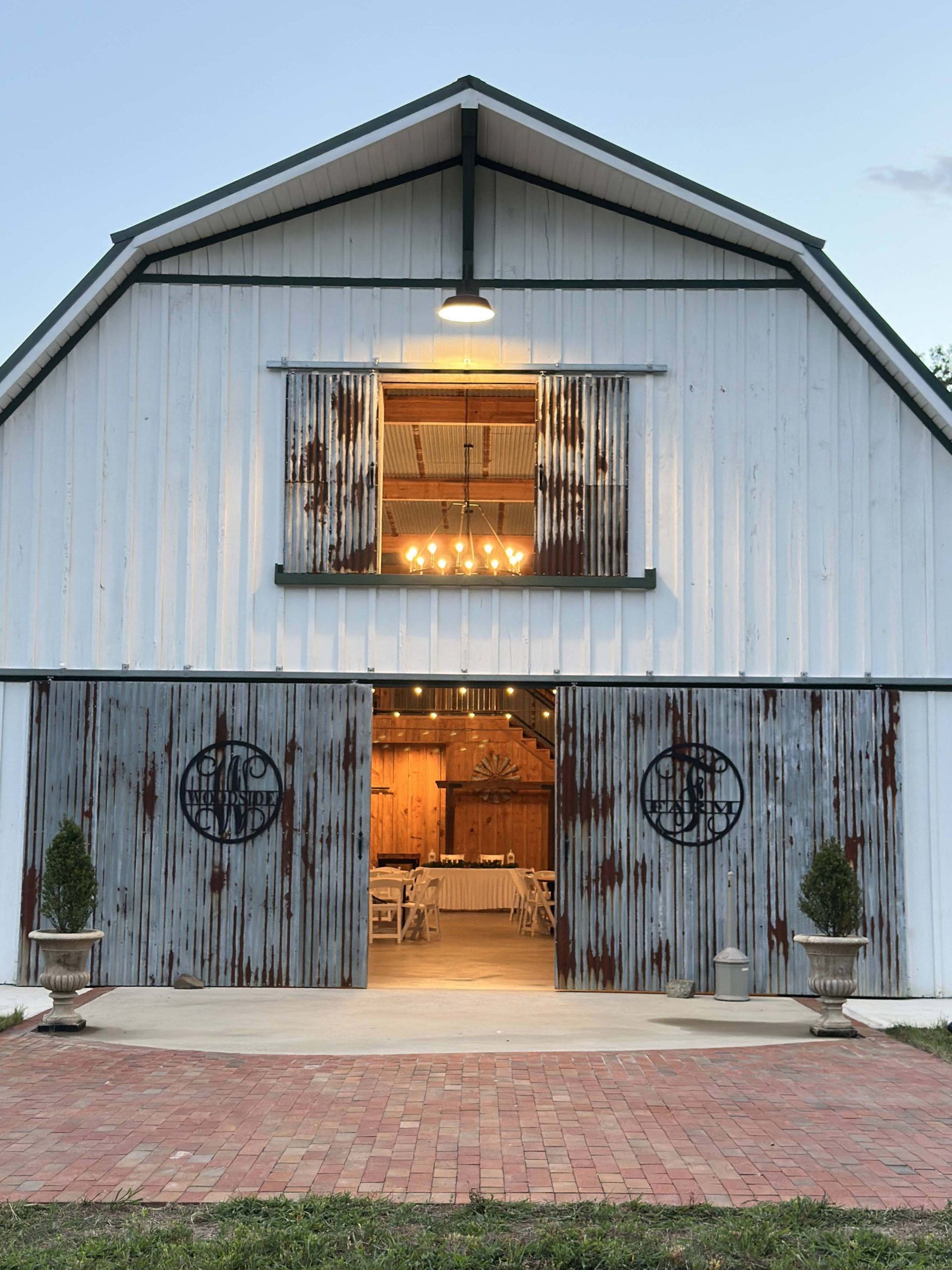 White barn-style building with open lit doorway, weathered double doors, and a brick path in front