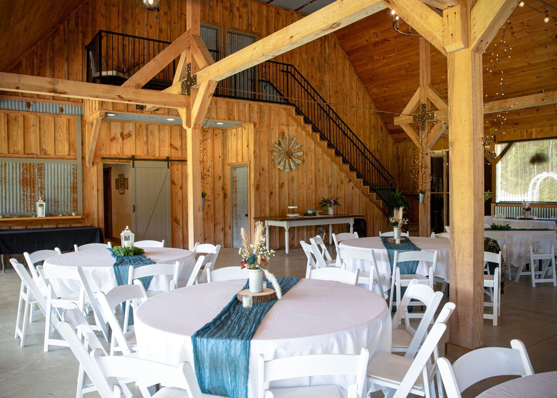 Rustic barn-style dining hall with round tables, white chairs, and wood beams