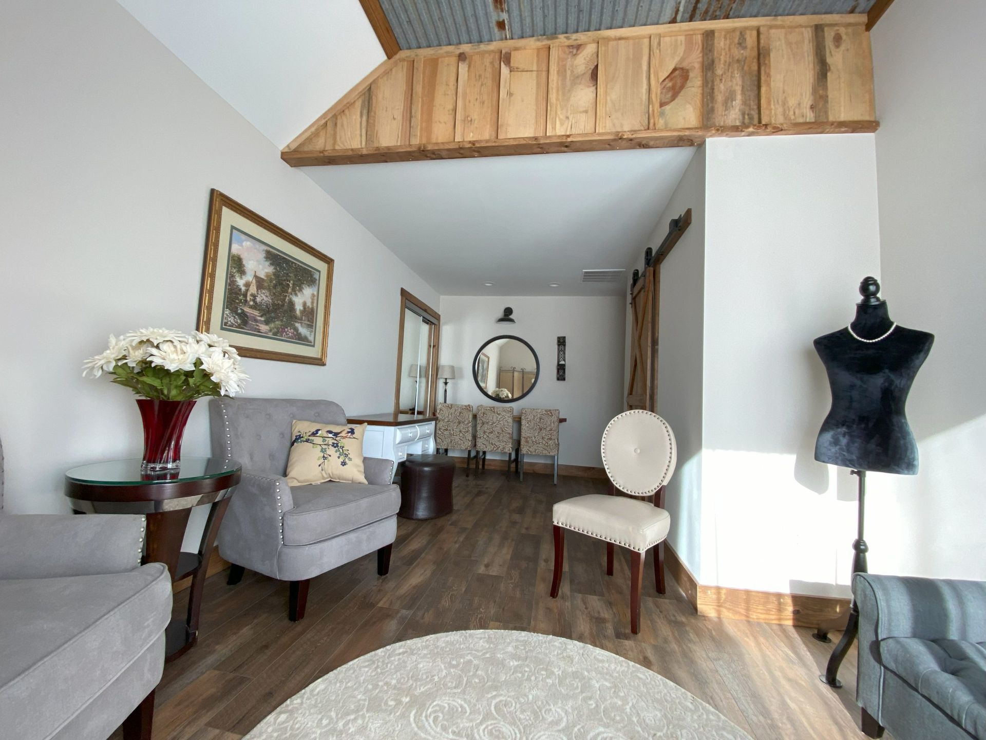 Bright living room with gray chairs, wooden loft railing, round mirror, and black dress form mannequin