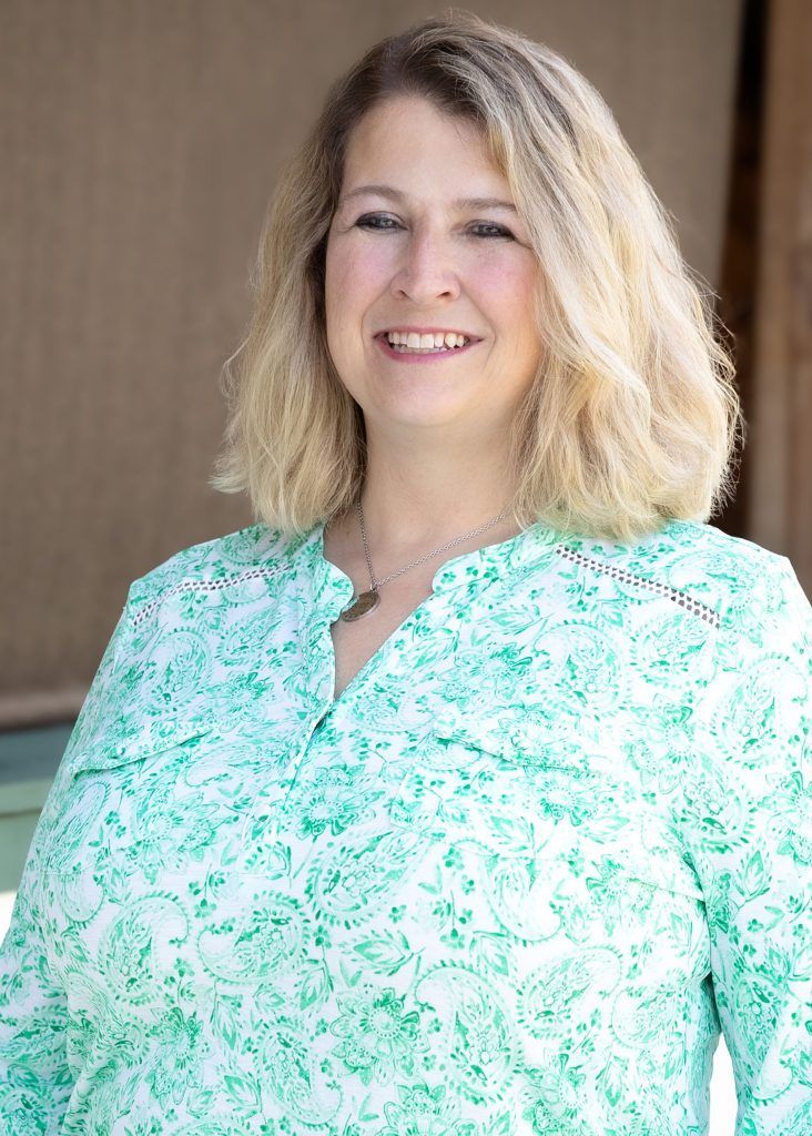 Smiling person in a mint green patterned blouse against a brown backdrop