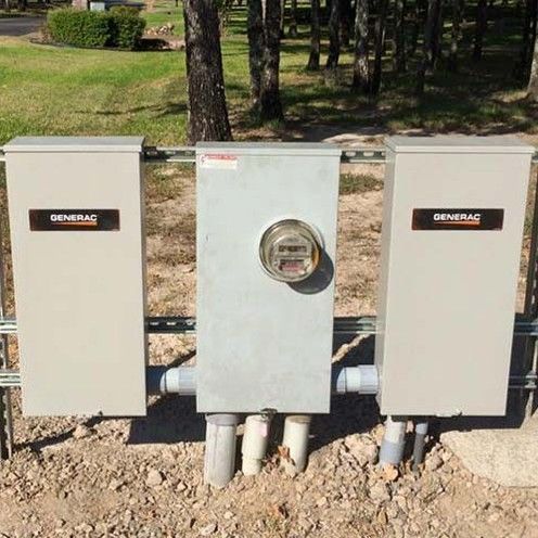 Three gray utility meter boxes outdoors on a dirt pad, with trees and grass in the background