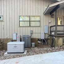 Outdoor HVAC units beside a beige house wall with window, chair, and gravel bed