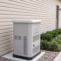 White utility cabinet beside beige siding and landscaping stones outdoors