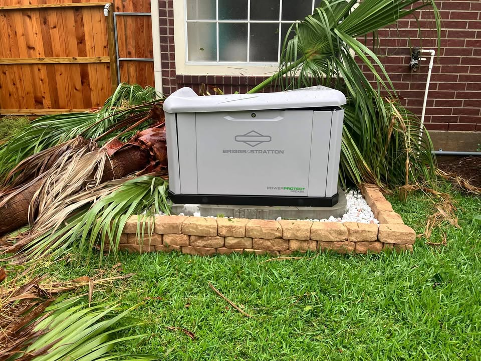 Portable gray generator on a brick pad beside a house, surrounded by fallen palm fronds and grass.