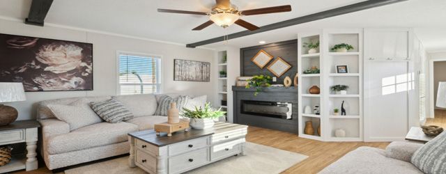 Bright modern living room with gray sectional, white shelves, ceiling fan, and coffee table