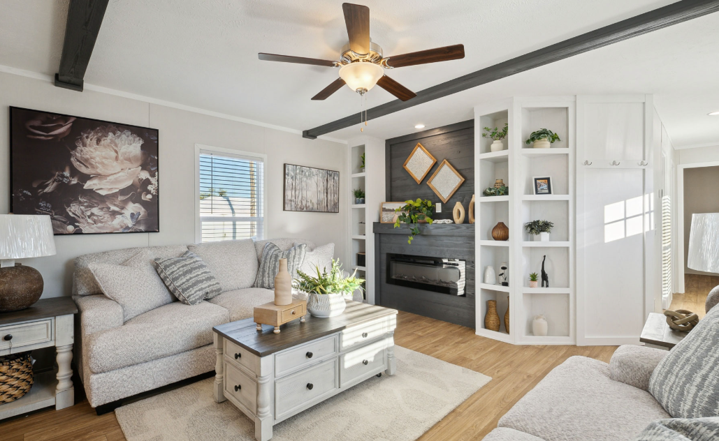 Bright living room with white sofa, ceiling fan, fireplace, built-in shelves, and neutral decor