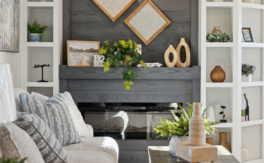Cozy living room with gray sofa, white built-ins, fireplace, greenery, and decorative wall art