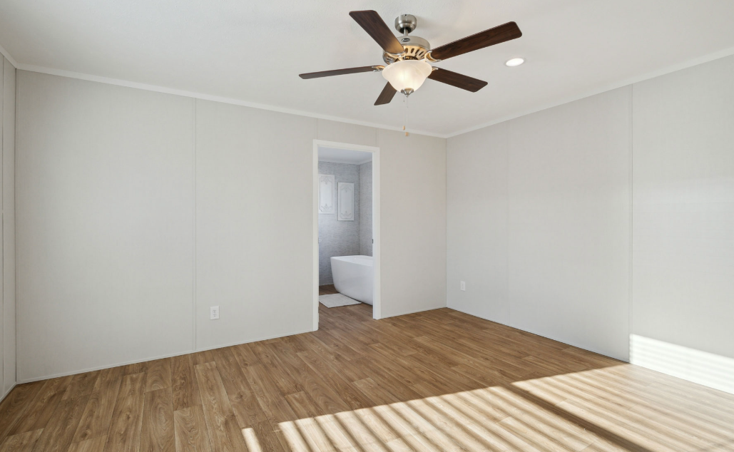 Empty white bedroom with wood floor, ceiling fan, and doorway to a bathroom