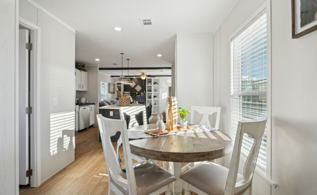 Bright dining room with a round table, white chairs, and sunlight streaming through large windows.