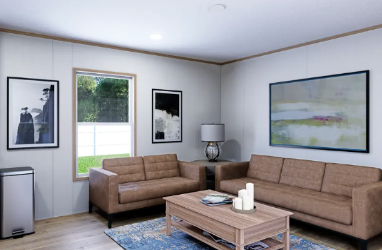 Modern living room with beige sofas, coffee table, blue rug, framed art, and a window with greenery outside